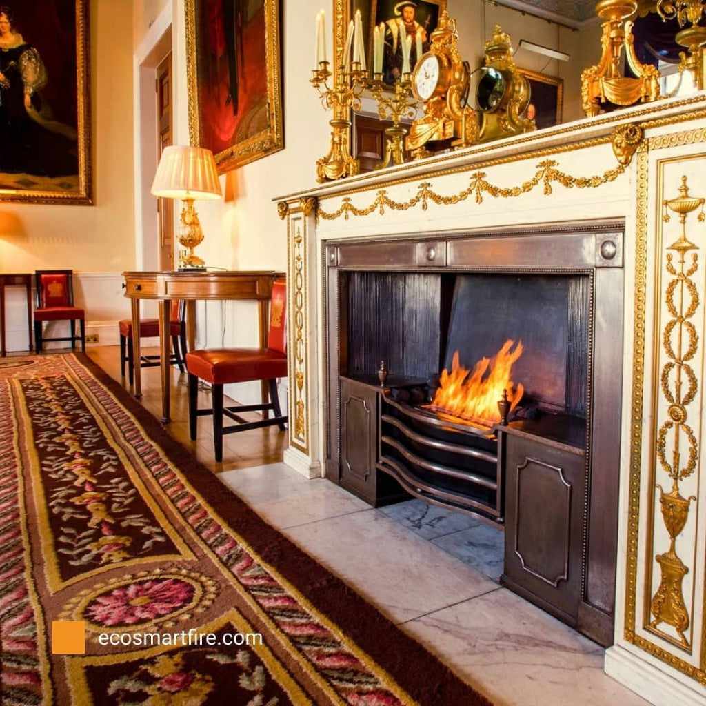 EcoSmart Fire Grate 30 installed in an ornate, traditional fireplace with a dark metal finish and glowing flames.