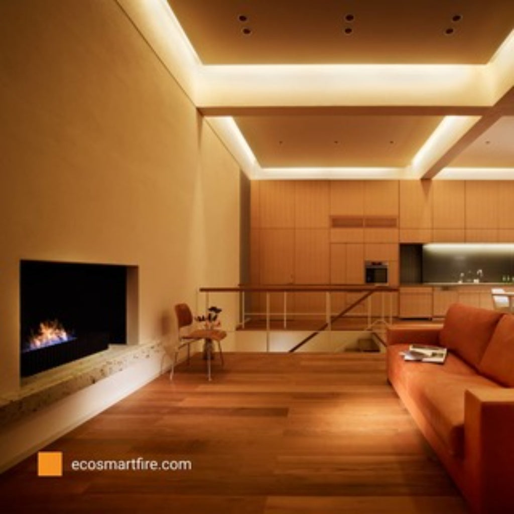 EcoSmart Fire Grate 36 installed in a modern living room with wooden floors, orange sofa, and warm recessed lighting.