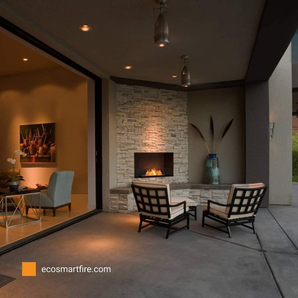 EcoSmart Fire Grate 36 installed in a stone fireplace on a modern outdoor patio with two armchairs.