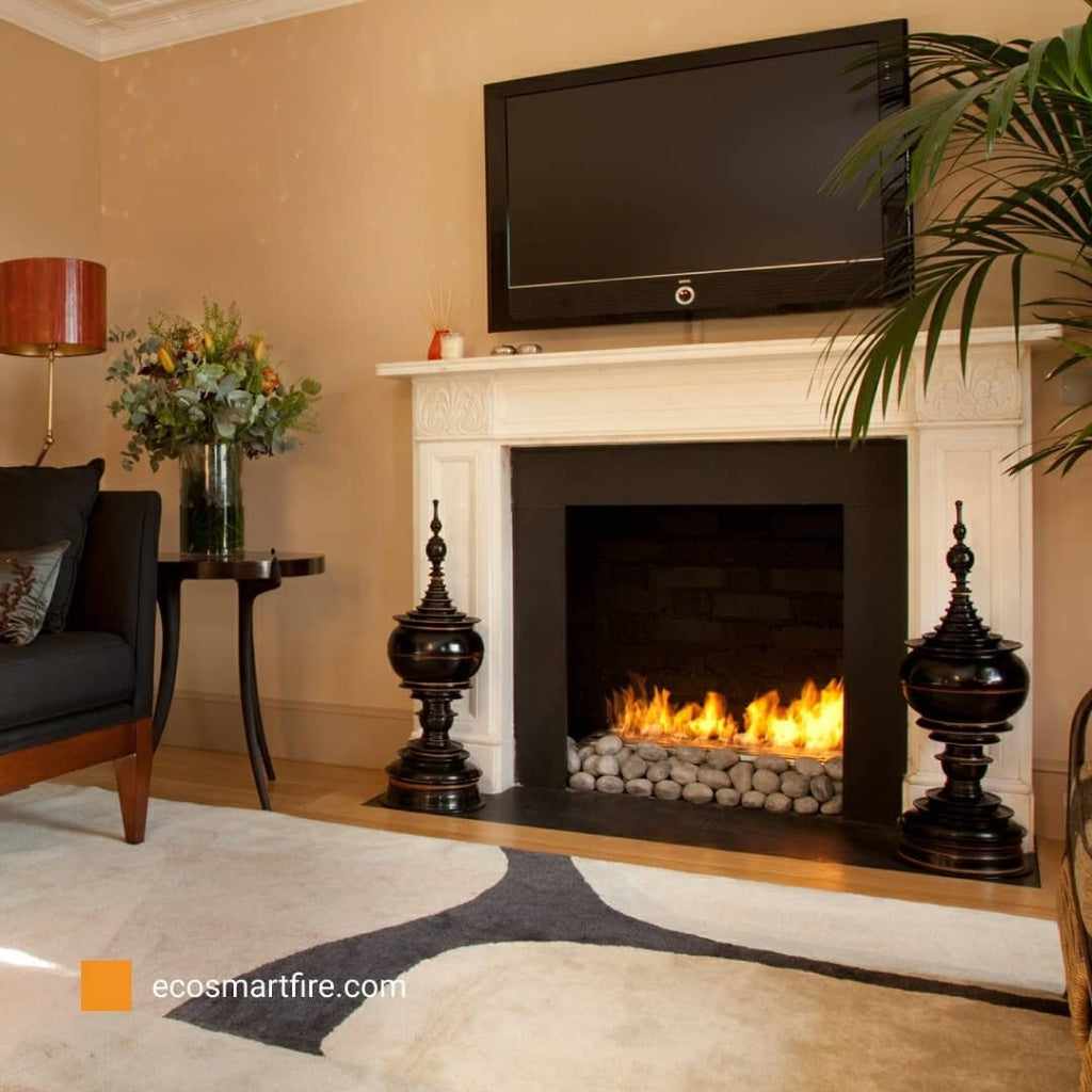EcoSmart Fire Grate 36 installed in a white fireplace with a pebble bed and flames, beneath a wall-mounted television.