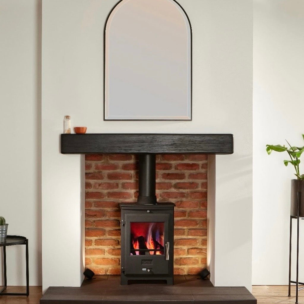 OER 5 MultiFuel 5KW stove in black, set in a brick fireplace with a dark wooden mantel and an arched mirror above.