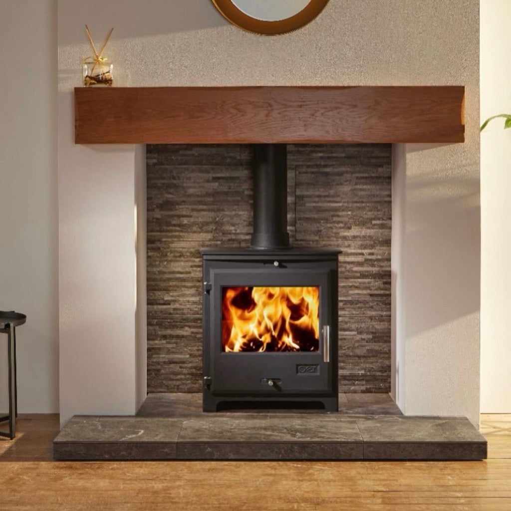 OER 8 MultiFuel stove in black with a burning fire, set in a stone-tiled fireplace with a wooden mantel beam.