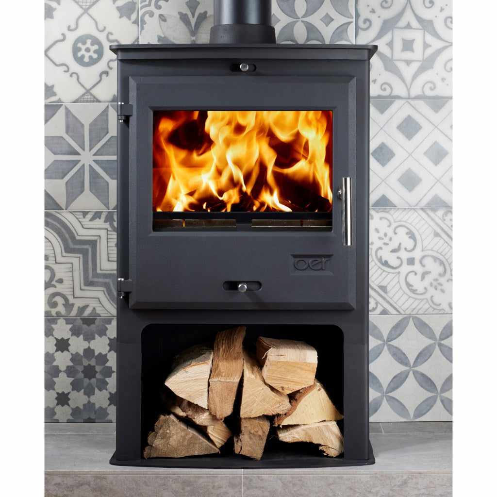 OER 8 MultiFuel 8KW wood burning stove in black with a lit fire and a log storage compartment against patterned tiles.