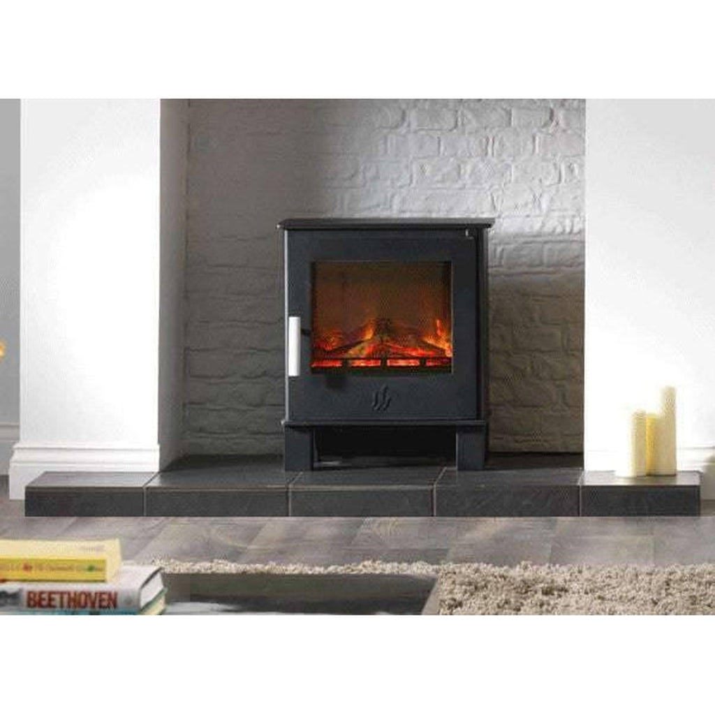 ACR Malvern HD electric stove in black with a glowing log flame effect, set on a dark tiled hearth against a brick wall.
