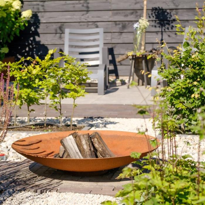 60cm Corten steel firepit bowl with a rustic orange finish, filled with logs in a sunny garden setting.