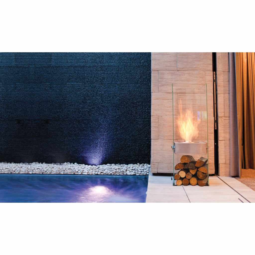 EcoSmart Fire Ghost bioethanol fireplace with glass sides and a log base, placed by a pool and dark stone wall.