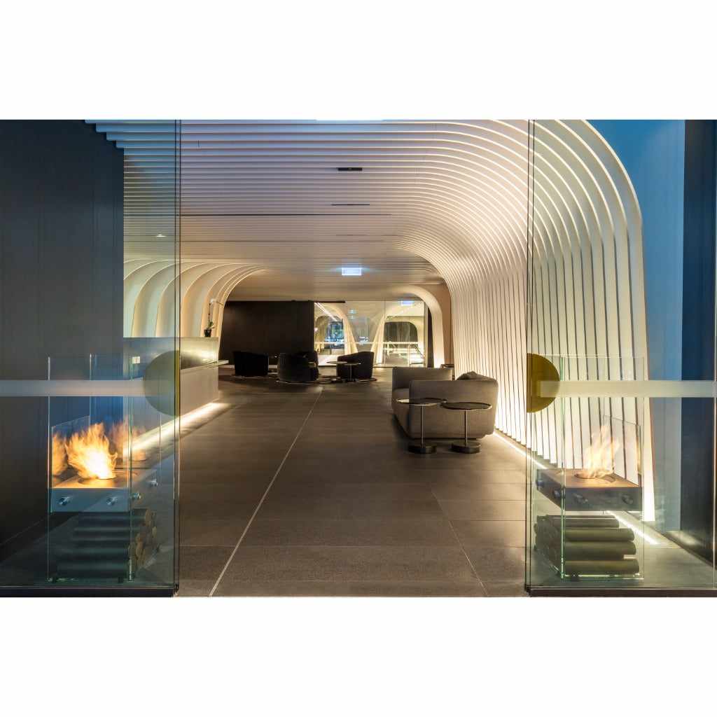 EcoSmart Fire Ghost bioethanol fireplace with glass panels and flames in a modern, curved architectural lobby.