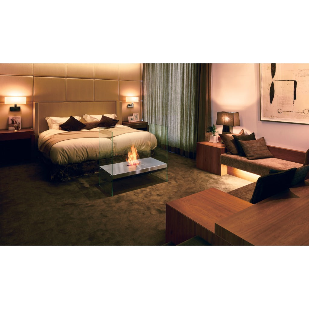 EcoSmart Fire Igloo bioethanol fireplace with a silver metal base and glass sides, glowing in a modern bedroom.