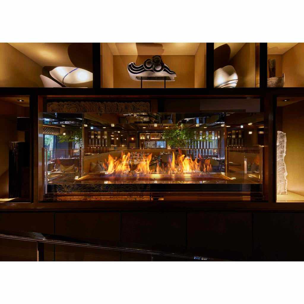 EcoSmart Fire XL1200 ethanol burner with a long, vibrant flame set behind a glass screen in a dark interior.