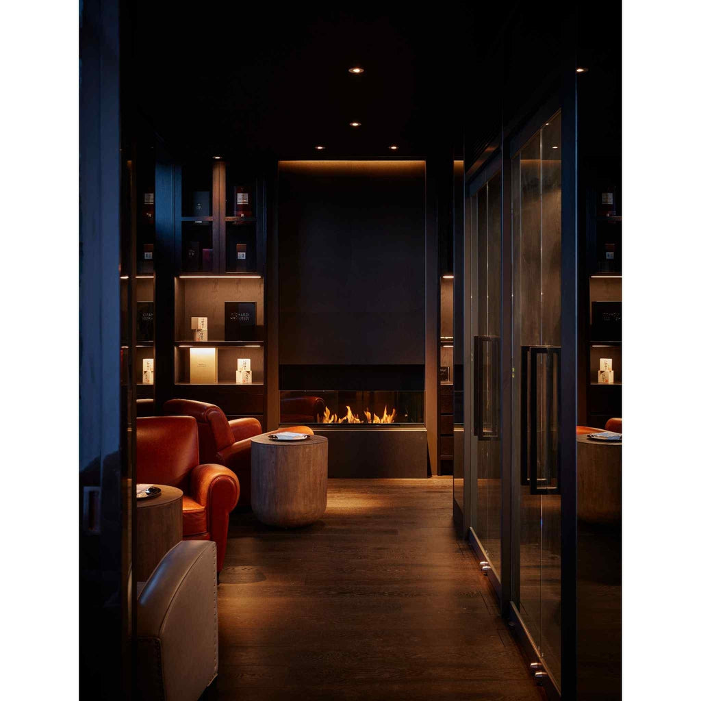 EcoSmart Fire XL900 ethanol burner glowing in a dark, modern lounge with leather armchairs and wooden flooring.
