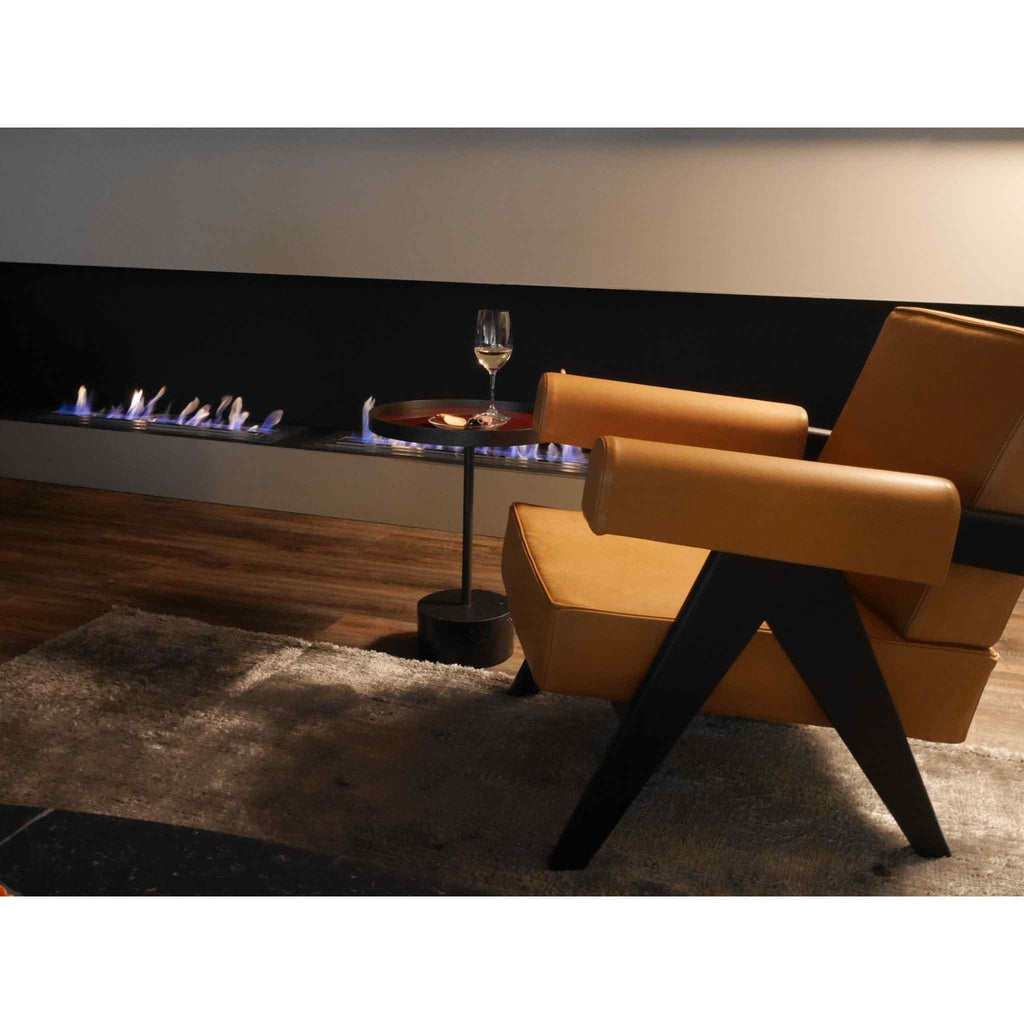 EcoSmart Fire XL900 ethanol burner with a long, linear flame set into a black wall above a tan armchair and side table.