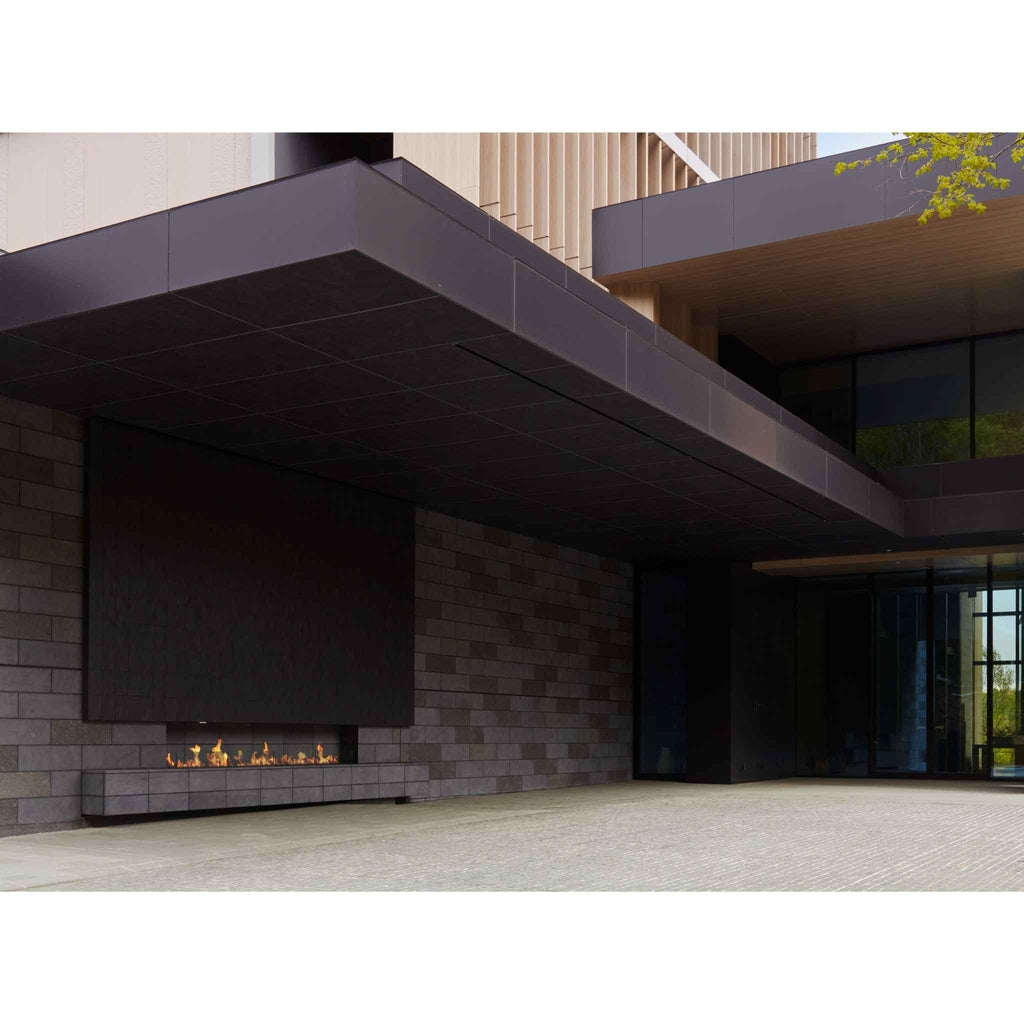 EcoSmart Fire XL900 ethanol burner integrated into a dark grey stone wall under a modern architectural canopy.