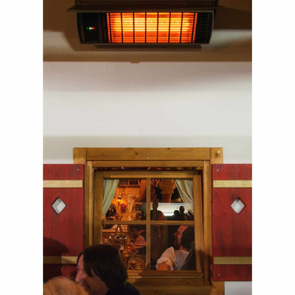 Heatscope Heaters Spot 2800W electric radiant heater mounted on a ceiling, glowing orange above a wooden window.