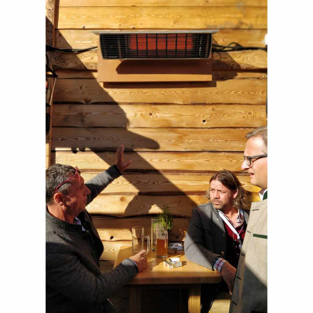Heatscope Heaters Spot 2800W electric radiant heater mounted on a wooden wall above three men sitting at a table.