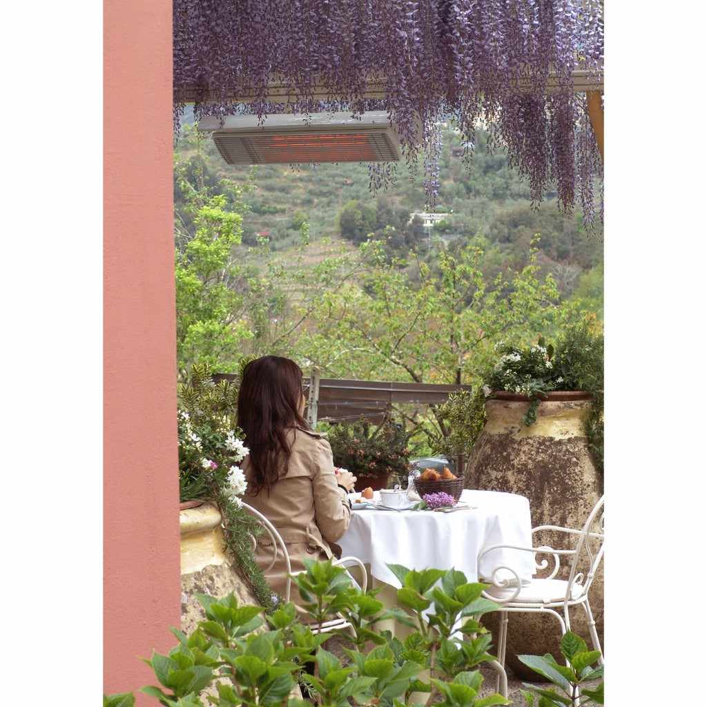 Heatscope Heaters Spot 2800W electric radiant heater mounted under a wisteria-covered pergola above a garden dining area.