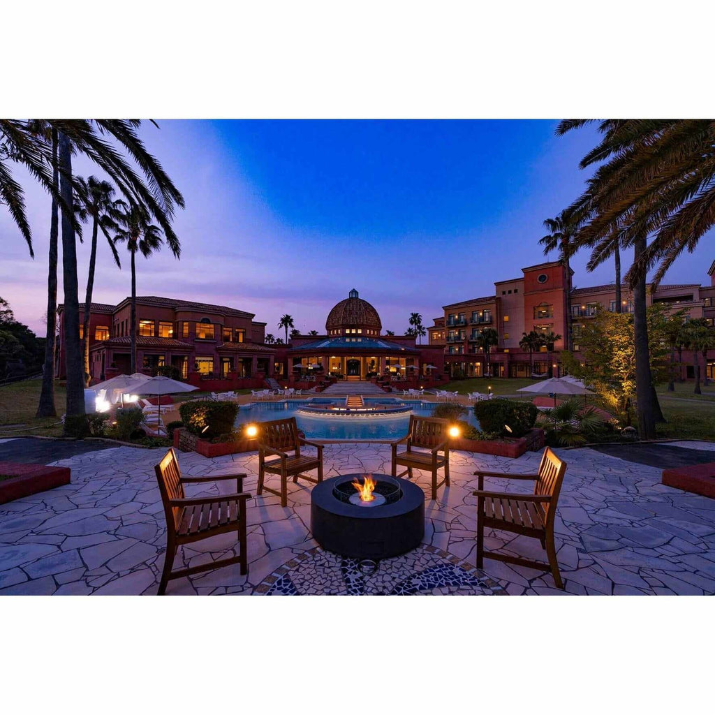 EcoSmart Fire Ark 40 bioethanol fire pit table in black, set on a stone patio with wooden chairs at dusk.