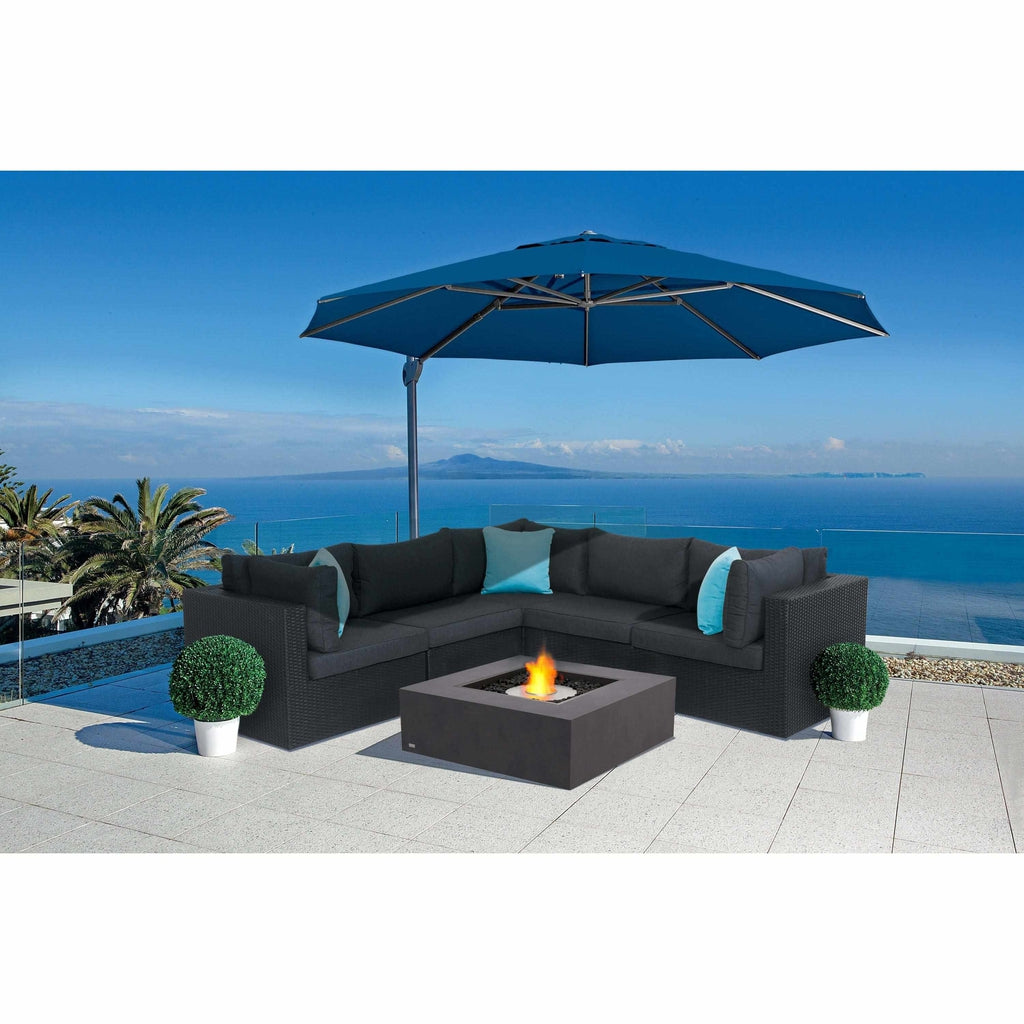EcoSmart Fire Base 40 bioethanol fire pit table in grey concrete with a lit flame, set before a black rattan sofa.