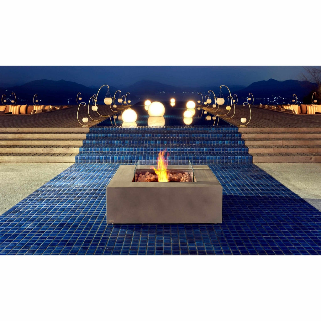 EcoSmart Fire Base 40 square concrete fire pit with a glass screen on a blue tiled patio at night.