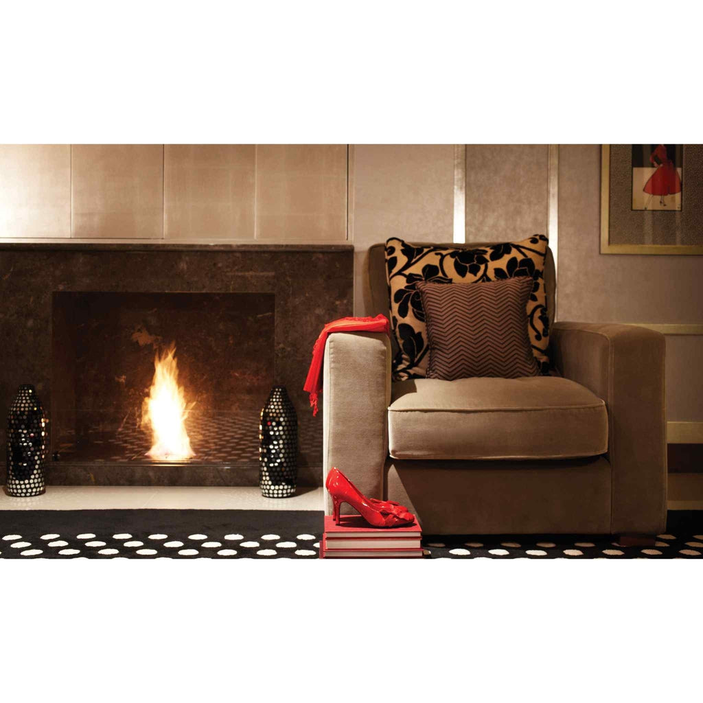 EcoSmart Fire BK5 ethanol burner with a bright flame inside a dark marble fireplace next to a beige armchair.