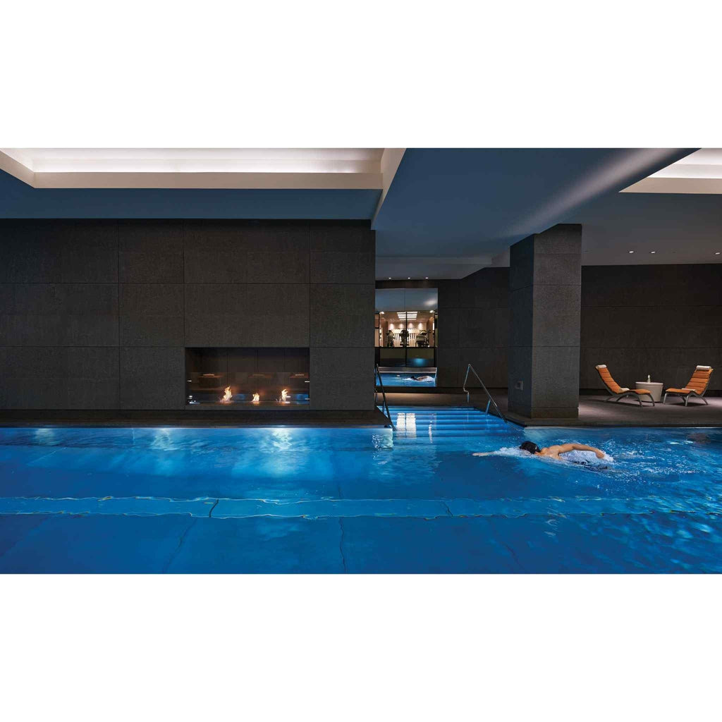 EcoSmart Fire BK5 ethanol burner integrated into a dark stone wall beside an indoor swimming pool.