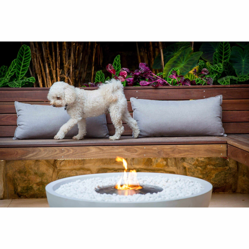 EcoSmart Fire Mix 850 bioethanol fire pit bowl with white stones and a flame, set on a patio with a wooden bench.