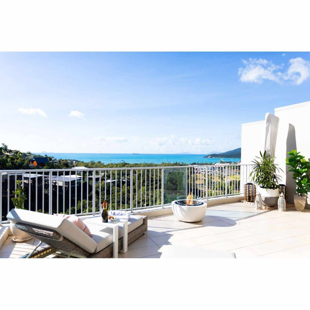 EcoSmart Fire Pod 30 bioethanol fire pit bowl on a sunny balcony overlooking a coastal view with a lounge chair.