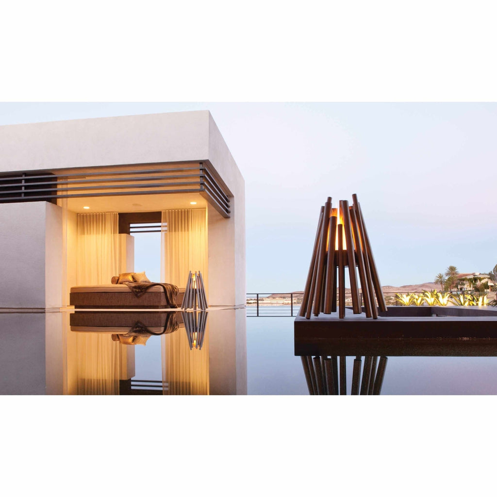 EcoSmart Fire Stix bioethanol fire pit with a brown, stick-like frame glowing on a patio by a reflective pool.