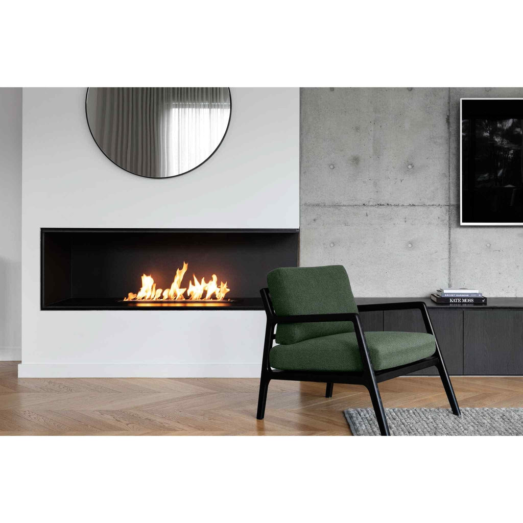 EcoSmart Fire XL700 ethanol burner with a linear flame in a black recessed wall mount above a green armchair.