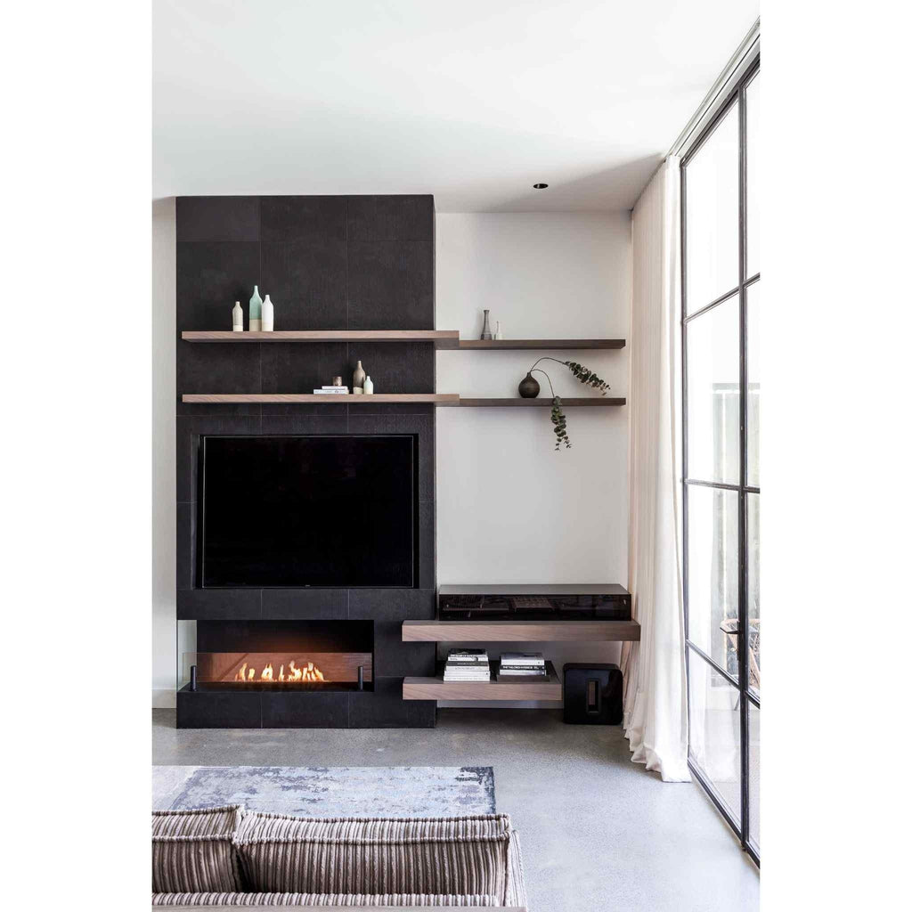 EcoSmart Fire XL700 ethanol burner integrated into a black tiled fireplace wall with floating wooden shelves.
