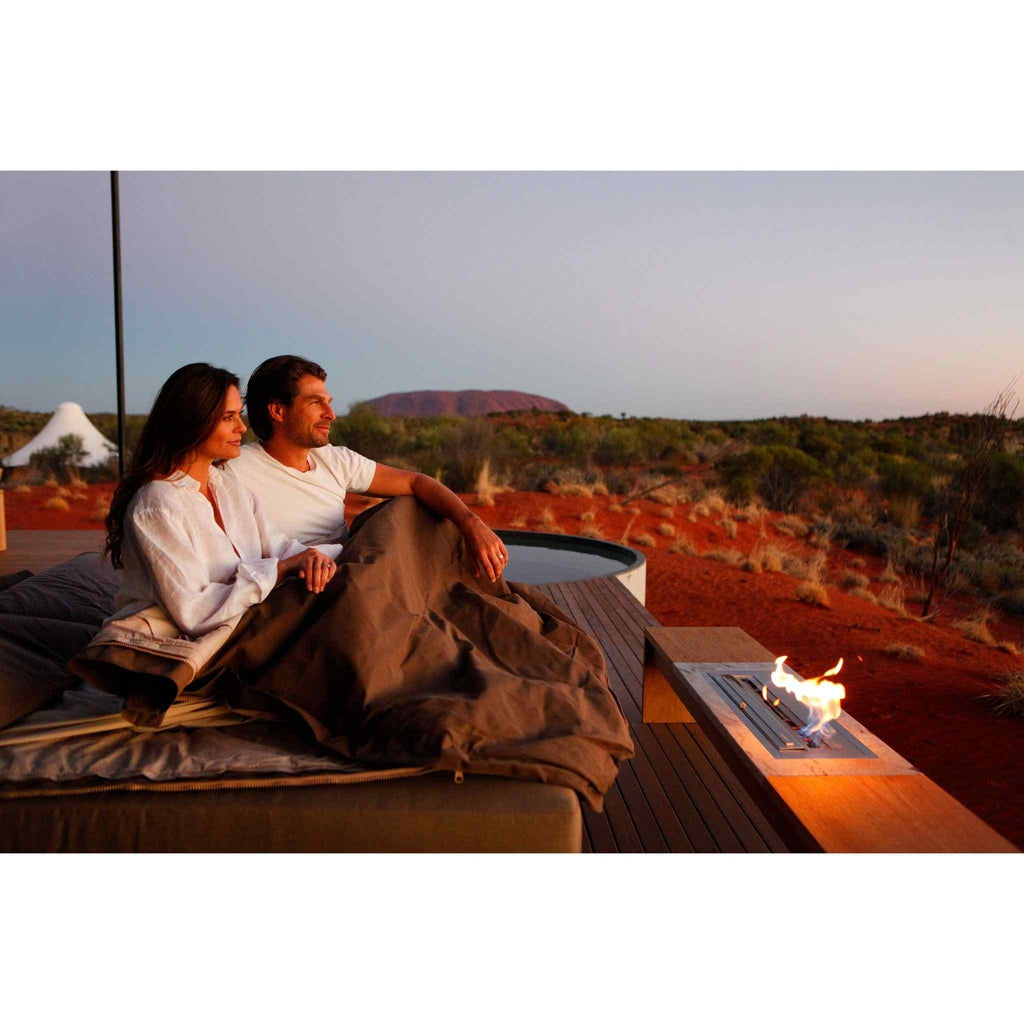EcoSmart Fire XL700 ethanol burner with a flame glowing on a wooden deck beside a couple in the Australian outback.