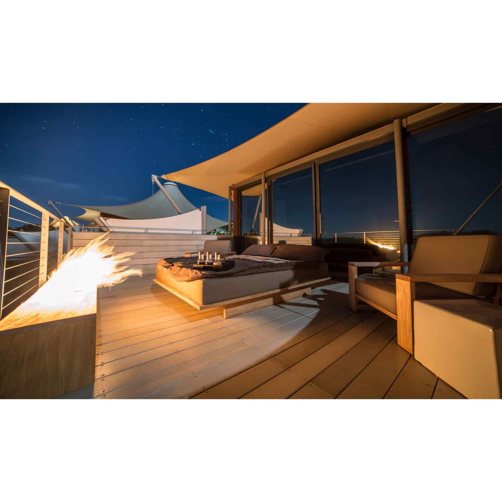 EcoSmart Fire XL700 Ethanol Burner with a bright flame on a wooden deck at night, next to an outdoor bed and chairs.