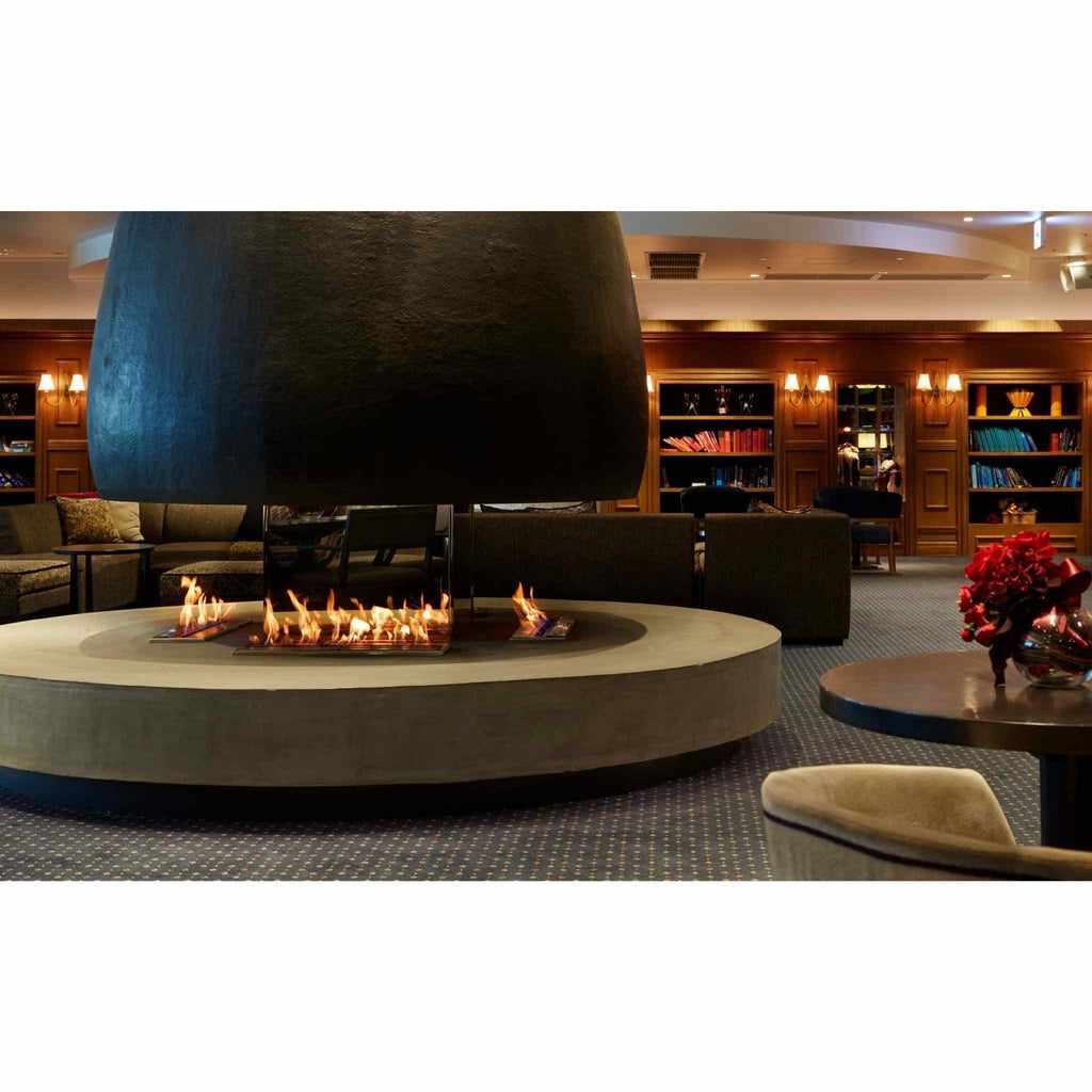 EcoSmart Fire XL700 ethanol burner inset into a circular concrete hearth with a large black suspended fireplace hood.