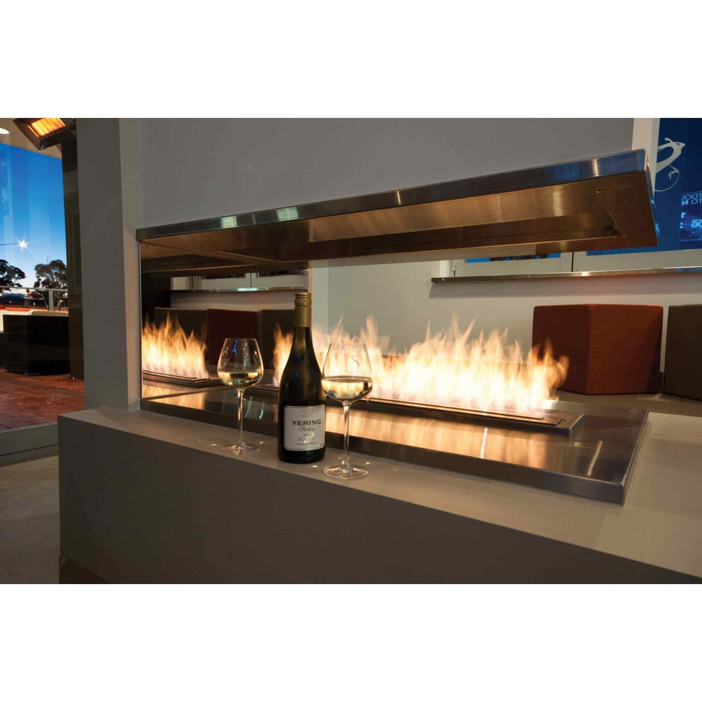 EcoSmart Fire XL900 ethanol burner with a long flame, stainless steel finish, and wine glasses on a modern hearth.
