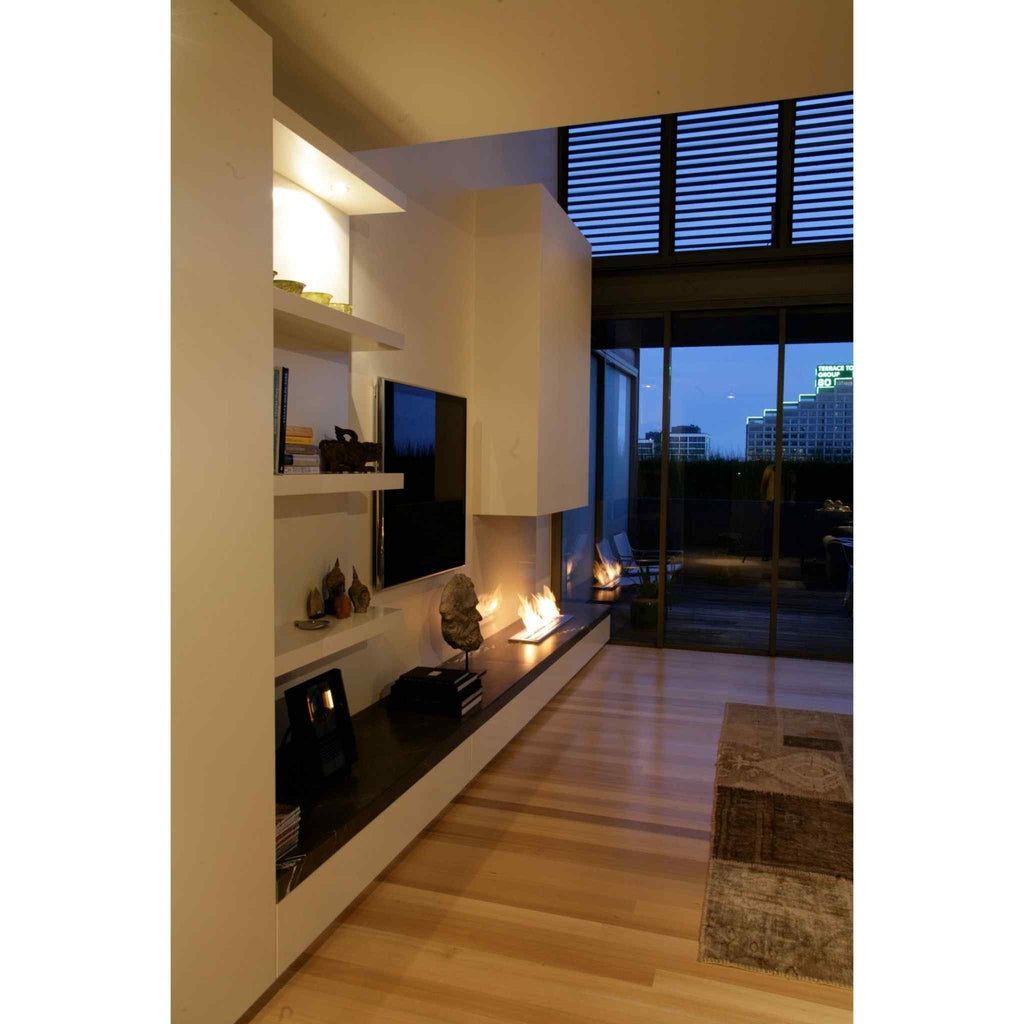 EcoSmart Fire XL900 ethanol burner integrated into a long, dark stone shelf in a modern living room with a flame lit.