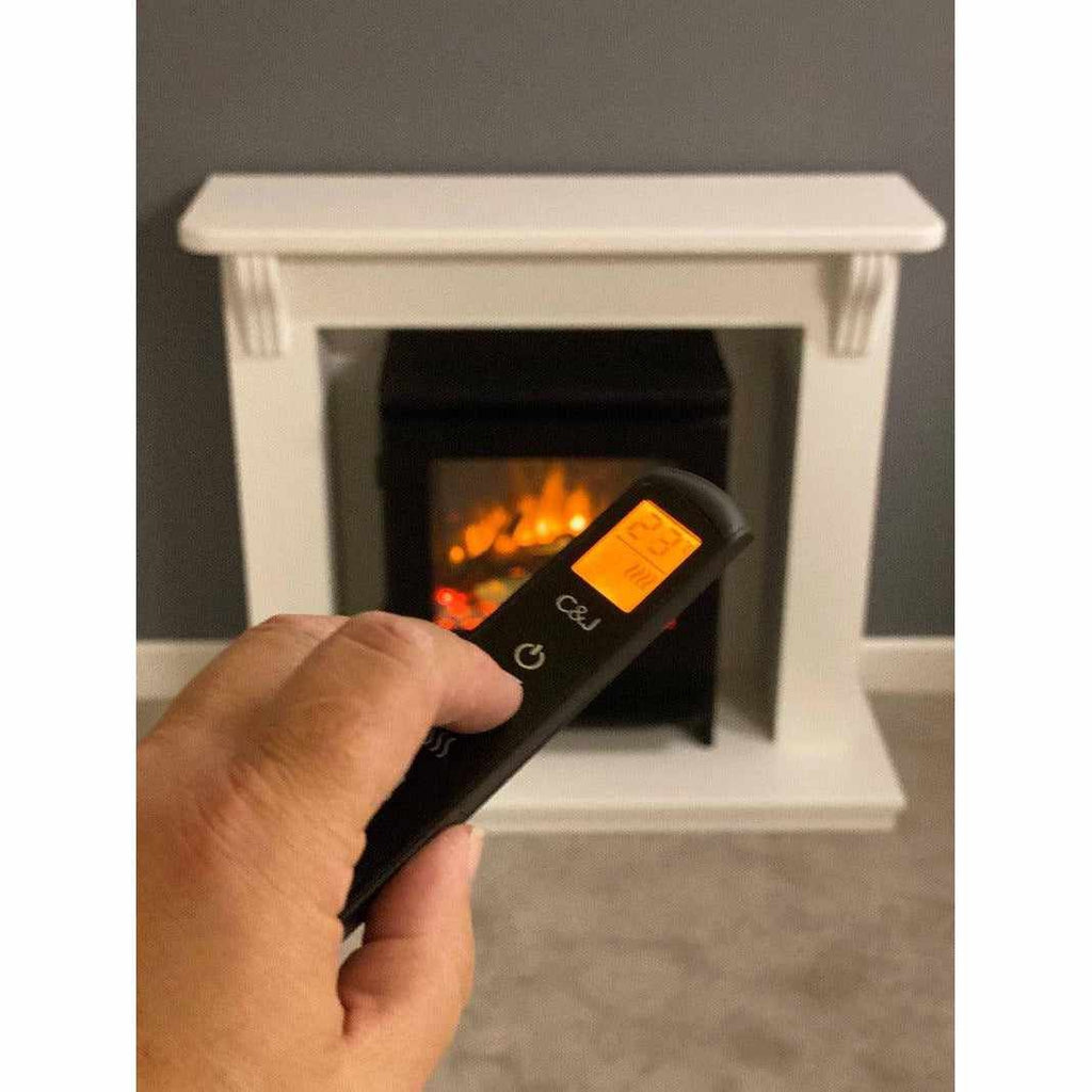 Hand holding a black remote control in front of a white Suncrest Ashby Electric Stove Suite with a glowing fire effect.