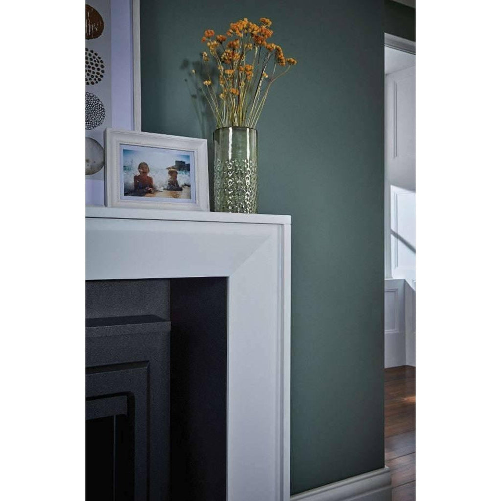 Suncrest Mayford Electric Stove Suite with a white surround against a dark green wall, featuring a vase and photo frame.