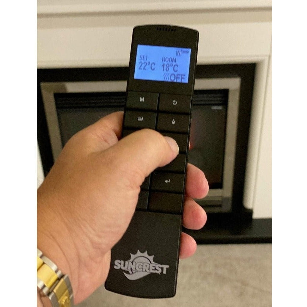 Hand holding a black Suncrest Middleton electric fireplace remote with a blue backlit digital display screen.
