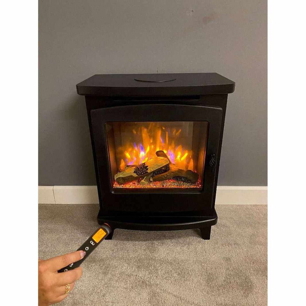 Suncrest Mitford electric stove in black with a glowing log flame effect, controlled by a handheld remote.